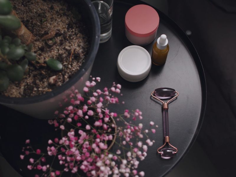 prikaz stola na kome je biljka u saksiji, roze cveće i prirodna kozmetika odja pored na istom stolčiću
