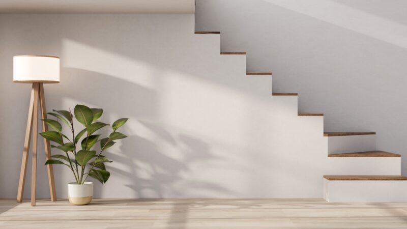 Minimalističko unutrašnje stepenište sa dekorativnom biljkom i podnom lampom pored zida