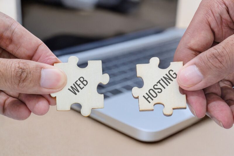 Ruke spajaju puzzle delove sa natpisima web i hosting ispred laptopa.
