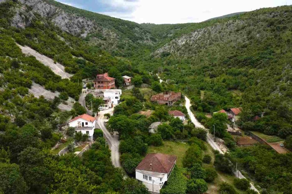 Pogled iz vazduha na malo selo smješteno u zelenoj dolini između brda i krševitih padina.