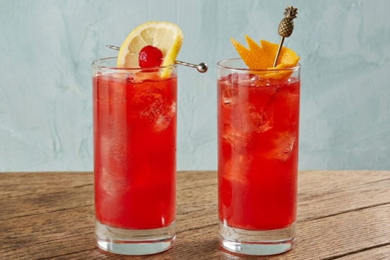 Dve čaše crvenog Singapore Sling koktela sa ledom i ukrasima od citrusa
